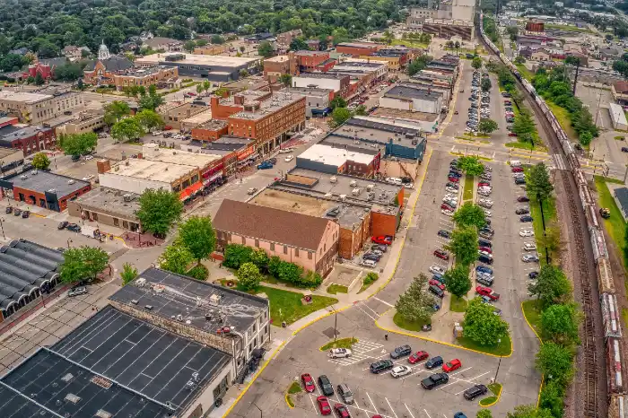 Aerial view of a small urban area with commercial buildings, parking lots, and a train track.