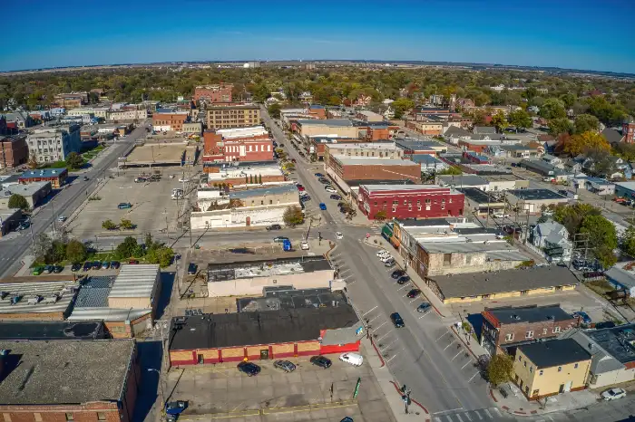 Aerial view of a small urban downtown area with streets, parked cars, and low-rise buildings under a clear blue sky.