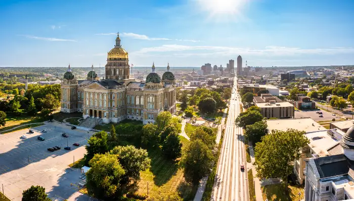 Aerial view of a historic capitol building with a golden dome and surrounding greenery under a clear blue sky.