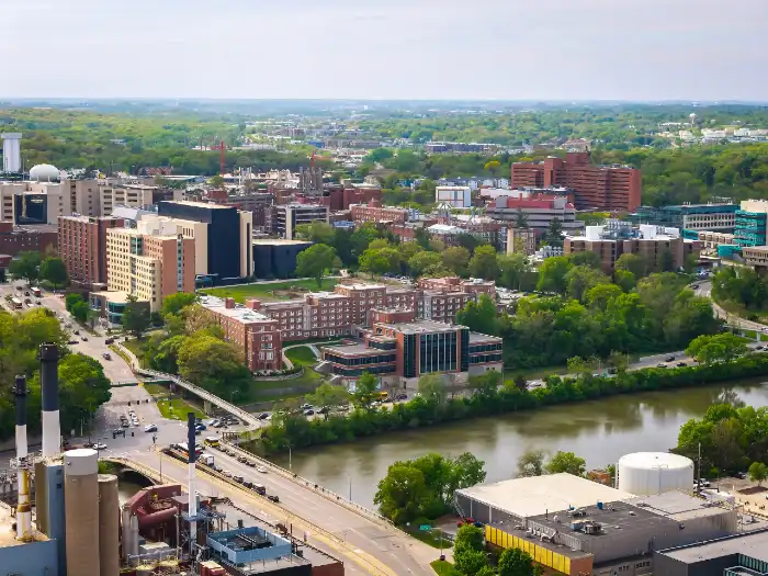 Aerial view of an urban area with buildings, a river, green trees, and roads.