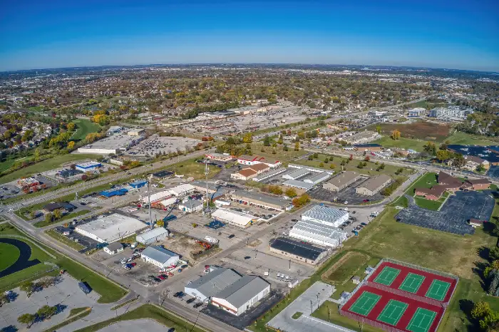 Aerial view of an industrial complex with warehouses, parking lots, and tennis courts under a clear blue sky.