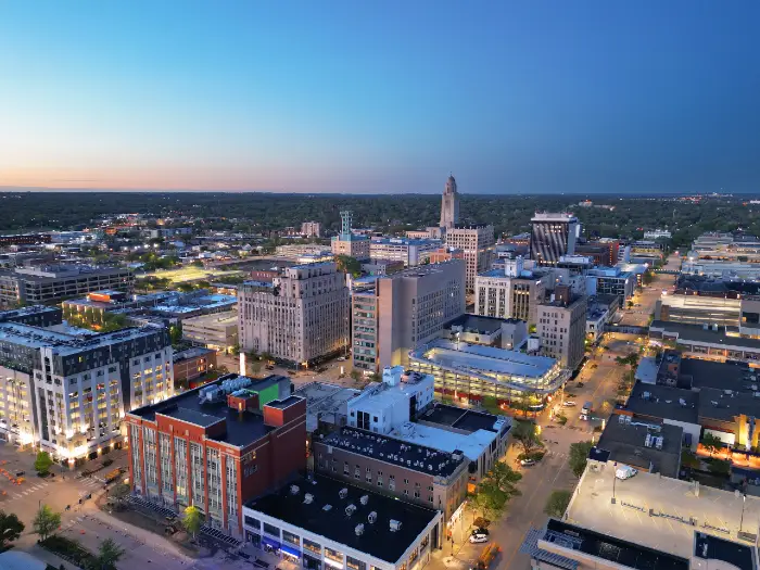 Aerial view of a mid-sized city skyline at dusk with illuminated buildings and clear sky.