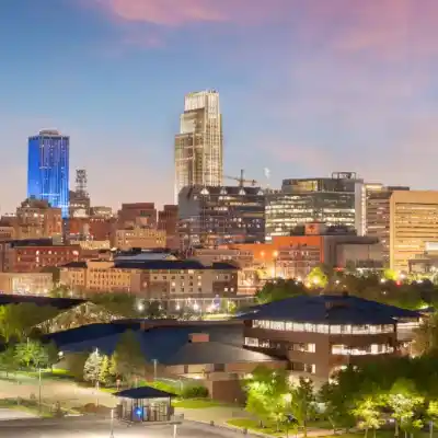 City skyline at dusk featuring illuminated modern buildings under a purple and pink sky.