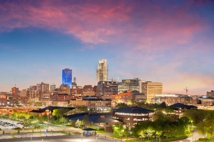 City skyline at dusk with illuminated buildings under a vibrant pink and purple sky.