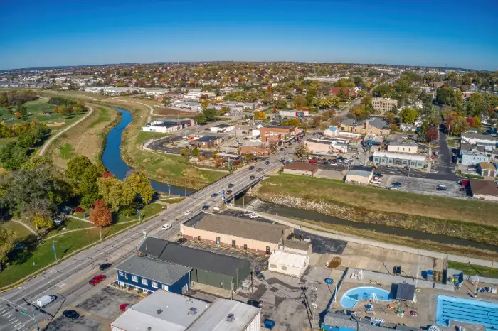 Aerial view of a small town with a river, bridge, roads, buildings, and autumn foliage.