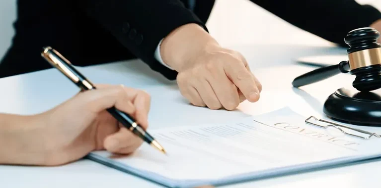 Hands of people reviewing a contract document with a judge's gavel and laptop on a white table.