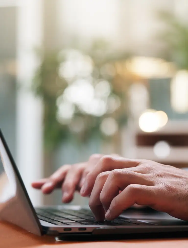 Close-up of hands typing on a laptop keyboard with a blurred indoor background.