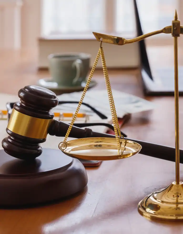 Close-up of a wooden judge's gavel and gold balance scales on a desk with blurred background.
