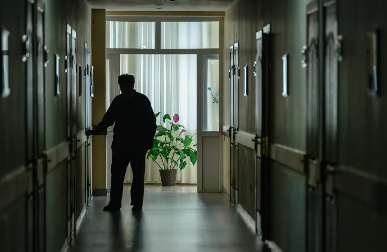 Silhouetted person standing in dimly lit hallway with closed doors and potted plant near window.