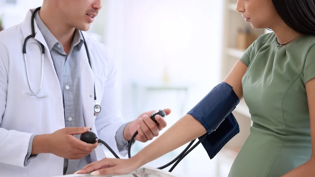 Doctor in white coat measuring blood pressure of woman wearing green dress with sphygmomanometer.