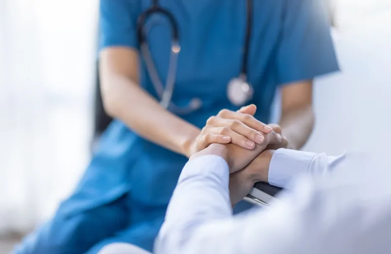Healthcare professional in blue scrubs comforting patient by holding hands.